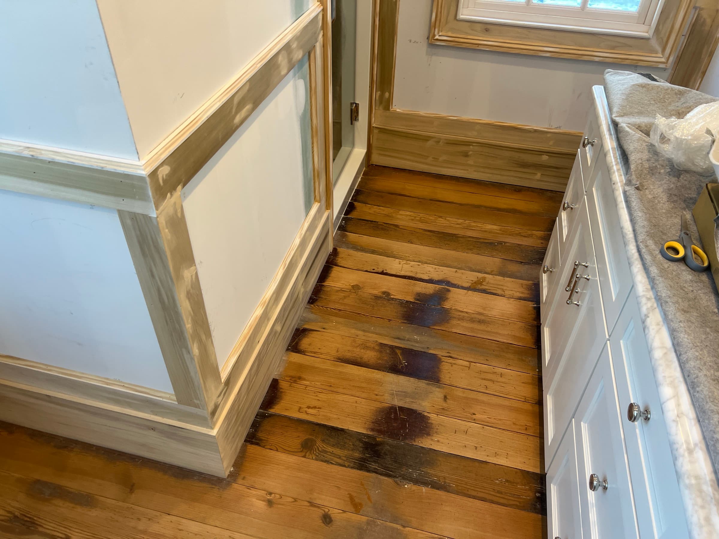 Heart pine floors mid-refinishing in Morrisville NC, dark water stains visible on wide plank pine during active renovation
