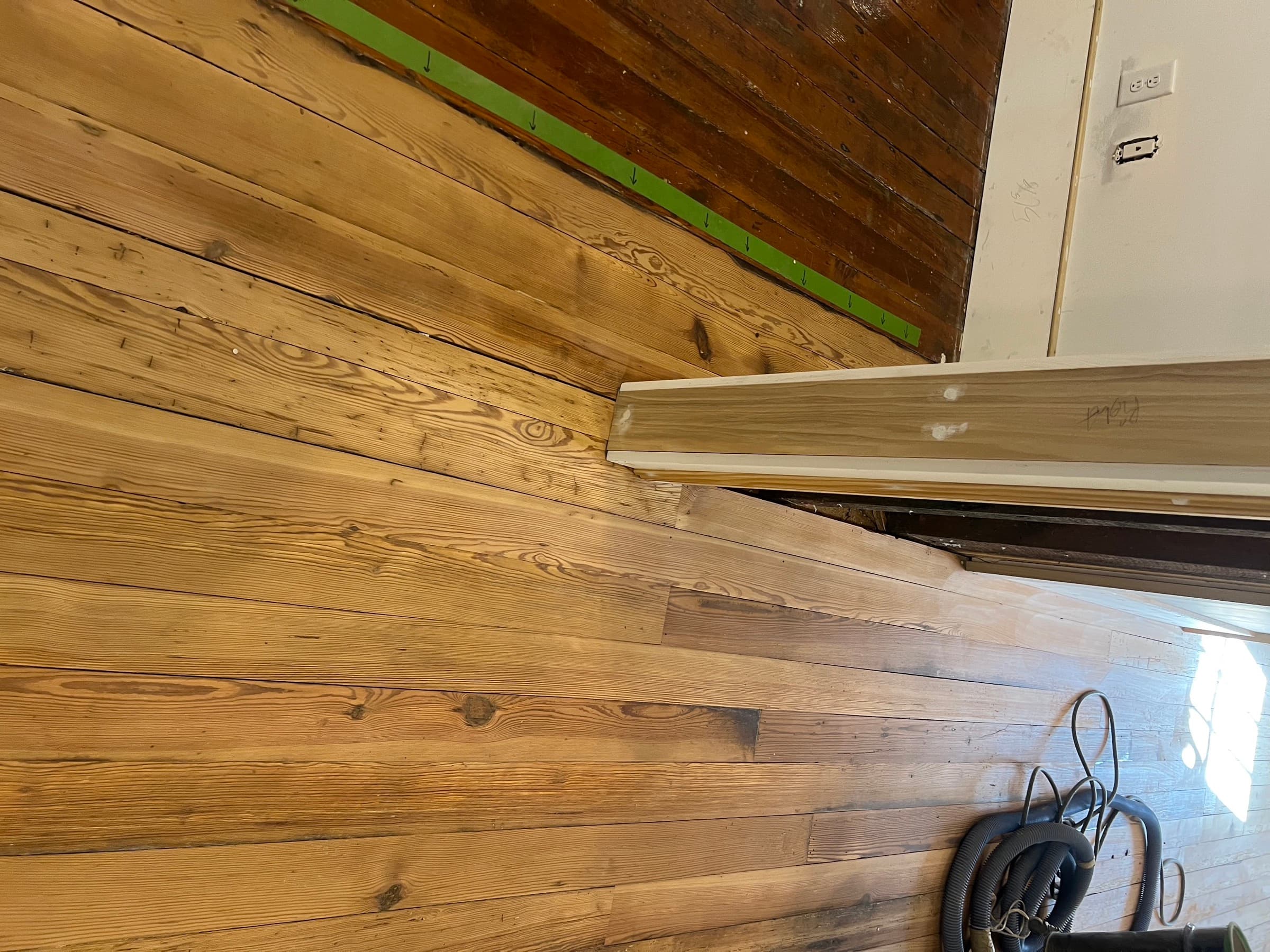Junction of original and salvaged patched heart pine boards during refinishing in Morrisville NC, green masking tape marking repair boundary
