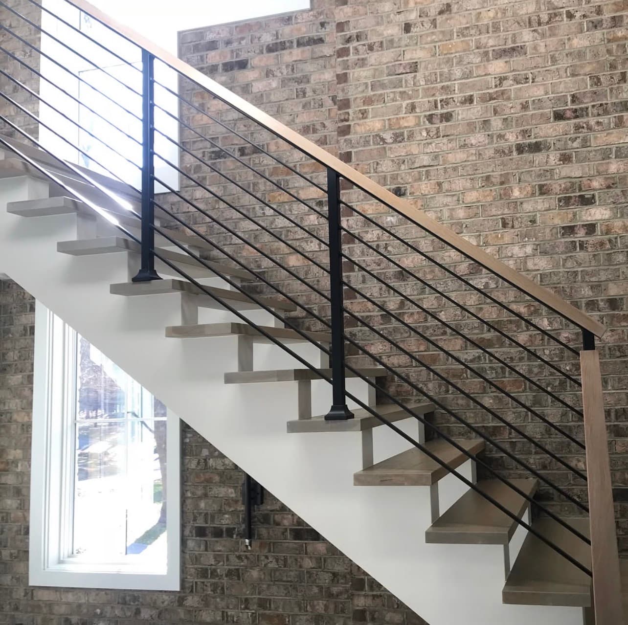 Staircase remodel with white oak floating treads and black horizontal rail against exposed brick wall Clayton NC